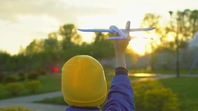 快乐的小男孩在日落时手持玩具飞机在公园里。孩子在户外夏天玩飞机。小飞行员梦想飞行，旅行度假幸福家庭大