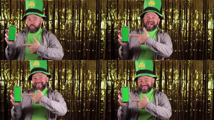 男性lepricon戴着一顶绿色的大三叶草帽子庆祝圣帕特里克节。指向智能手机的空白屏幕。