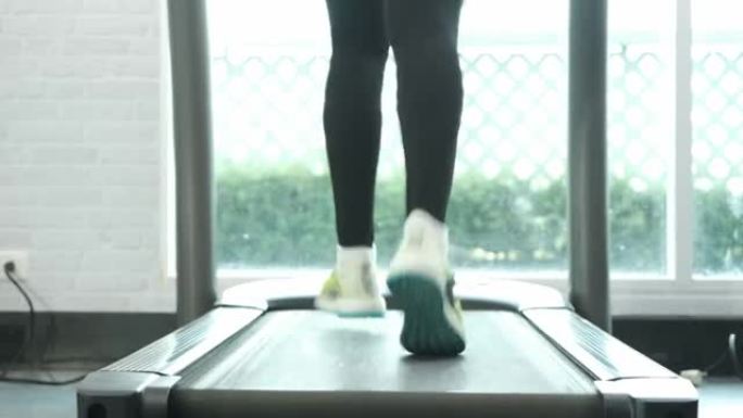 特写脚健身亚洲女子在跑步机上跑步后视摄像头，在健身馆进行马拉松比赛训练