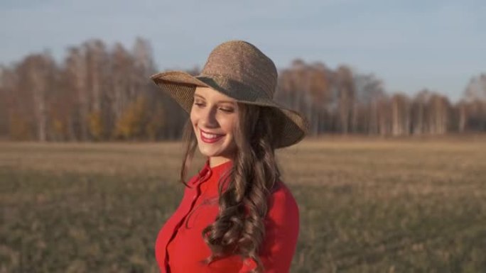 年轻快乐美丽的微笑女人穿着红色连衣裙和帽子，带着复古手提箱，在户外散步在夏天的乡村道路上