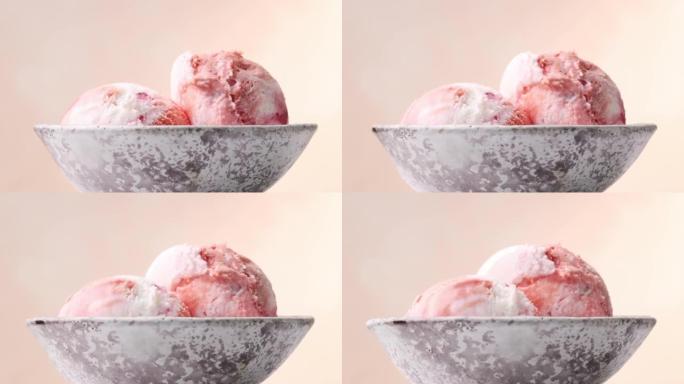 在米色背景上旋转的碗中，两个粉红色水果冰淇淋球的特写镜头