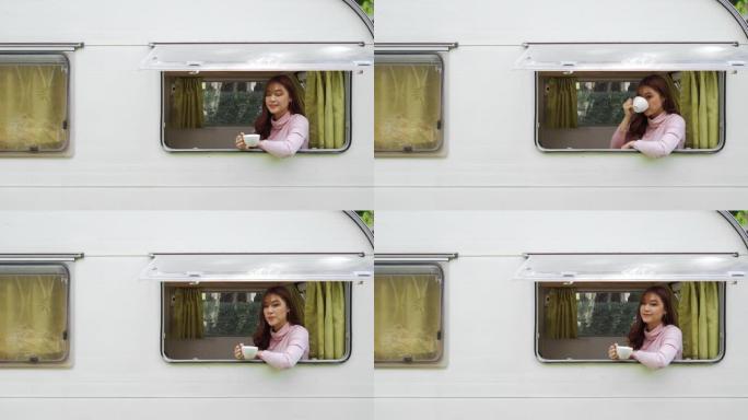 快乐的年轻女子在露营车房车的窗户上喝咖啡
