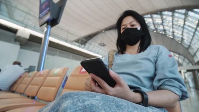 亚洲女性旅行者在机场航站楼等待出发时使用手机，当旅行泡沫出现在新的正常社交距离生活方式中