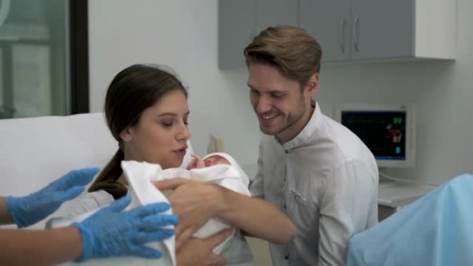 助产士将新生婴儿交给母亲抱，在医院的妻子附近支持父亲。幸福的家庭。分娩，父母，妇女，产妇，怀孕，产科