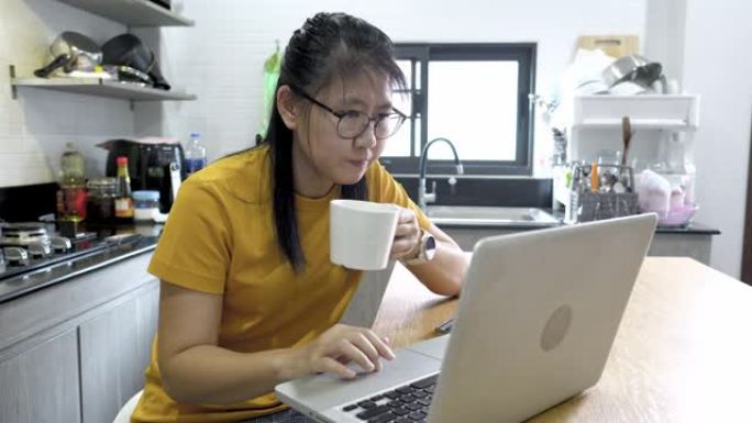 亚洲女性自由职业者使用笔记本电脑在家里的厨房里工作。