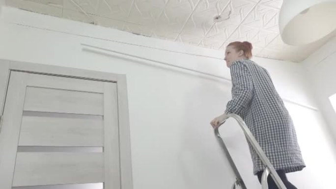 一名妇女爬上梯子，在天花板底座上尝试伸展天花板，用自己的双手修理