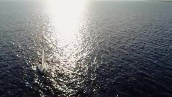帆船在阳光的照射下在海中航行。我们可以看到船和水在地平线上的整个和光线的反射-用无人机4K鸟瞰图