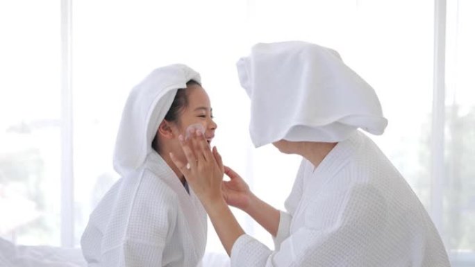 母亲在洗完澡后在卧室里放松，在女儿的脸上涂抹瑕疵霜。家庭美容治疗。青少年皮肤问题。
