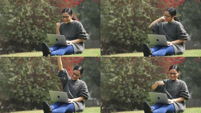 成功的女人坐在公园的草地上在笔记本电脑上工作