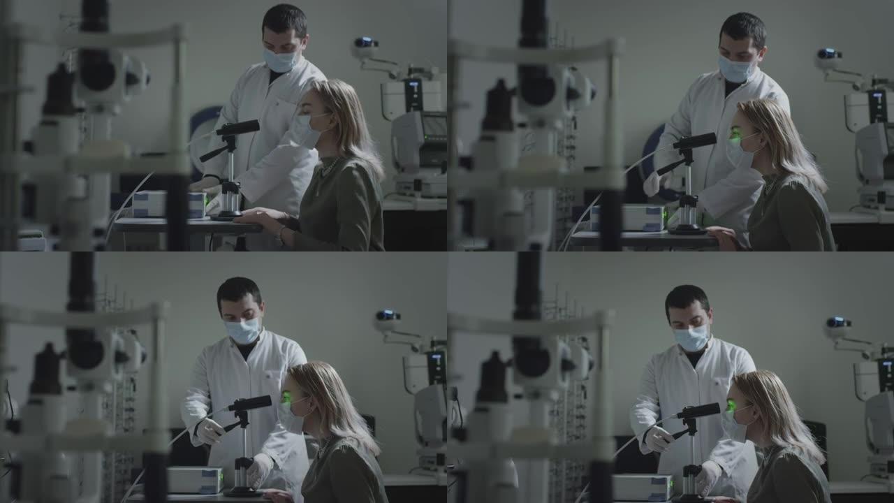 一位戴着医用防护口罩的妇女在眼科医生的预约下检查她的眼睛。一束绿色的激光射进瞳孔。眼科治疗-一位年轻