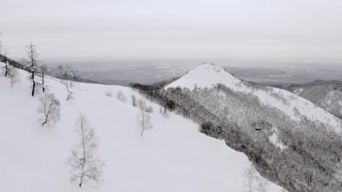日落时冬季白雪皑皑山脉景观的鸟瞰图。山边的黑暗树木森林。慢动作