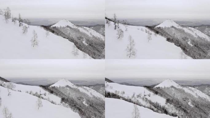 日落时冬季白雪皑皑山脉景观的鸟瞰图。山边的黑暗树木森林。慢动作