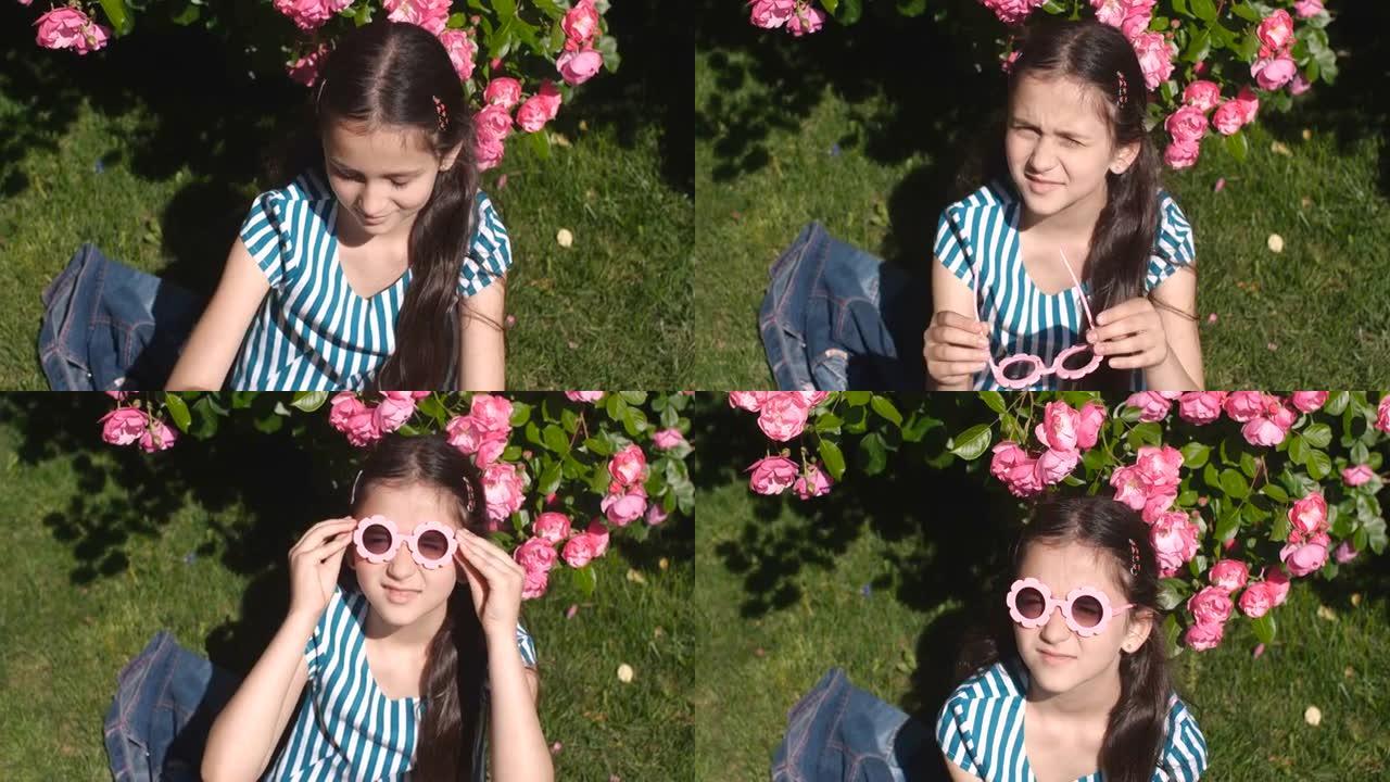 八岁的白人女孩，穿着条纹t恤的长发，坐在草地上，在刺眼的阳光下眯着眼睛，在开花的玫瑰丛中戴上眼镜。4