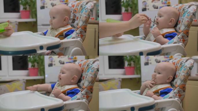 妈妈在家里的厨房里给小婴儿喂粥。8个月大的婴儿坐在高脚椅上，用勺子吃饭。婴儿食品概念。特写镜头。