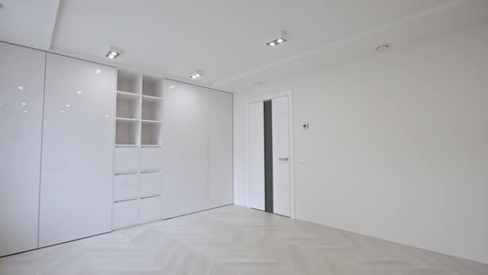 空置的无家具房间内部，配有木制人字形镶木地板，白色墙壁和天花板被筒灯照亮