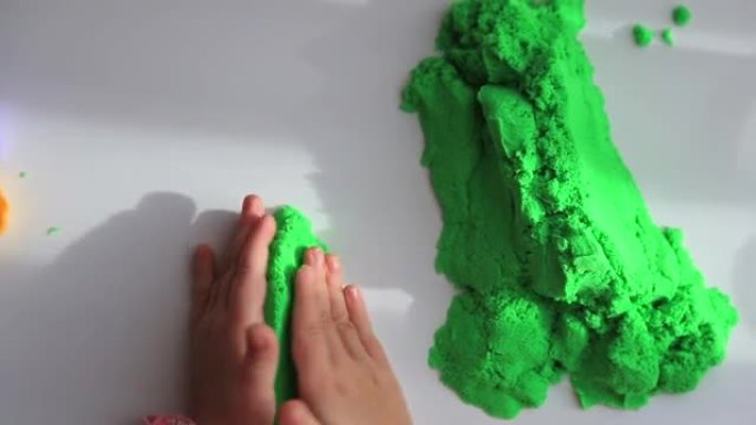 儿童在白色桌子上玩绿色运动沙的手的特写; 选择性聚焦