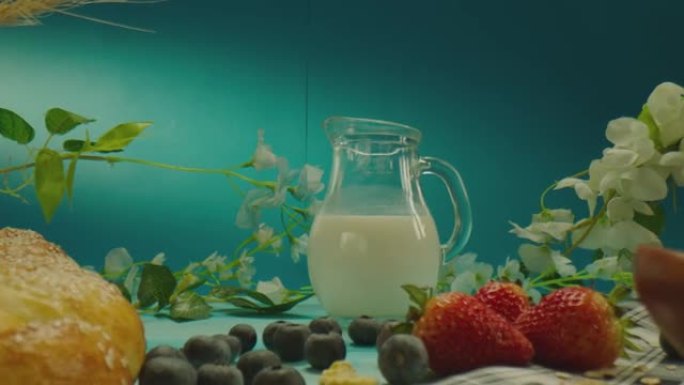 装饰桌子的美丽组成与牛奶乳制品，面包店，浆果，蓝色背景上的花朵。在慢动作的ARRI相机上近距离拍摄的
