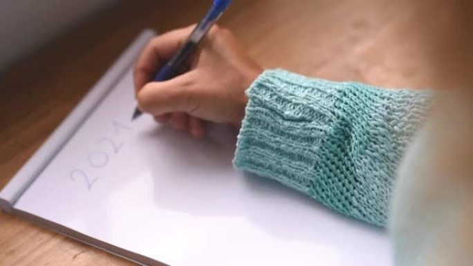 一个穿着蓝色衬衫或毛衣的女人的手特写，用笔在纸上写下她的2021目标