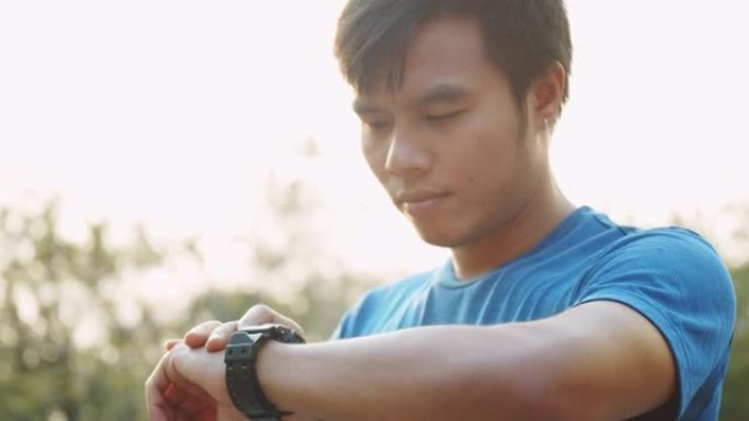 亚洲运动男子在公园的晴天进行训练锻炼后，使用健身追踪器或智能手表。