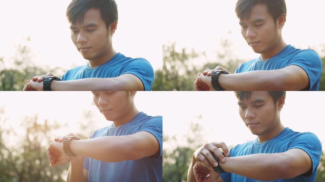 亚洲运动男子在公园的晴天进行训练锻炼后，使用健身追踪器或智能手表。
