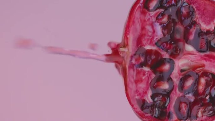 垂直视频。果汁滴从粉红色工作室背景下的天然石榴流出，带有复制空间，新鲜维生素