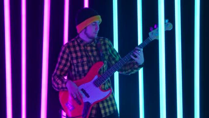 一位兴奋的吉他手在被粉红色和蓝色霓虹灯管包围的工作室里演奏电吉他。喜欢摇滚音乐的知足者。特写。慢动作