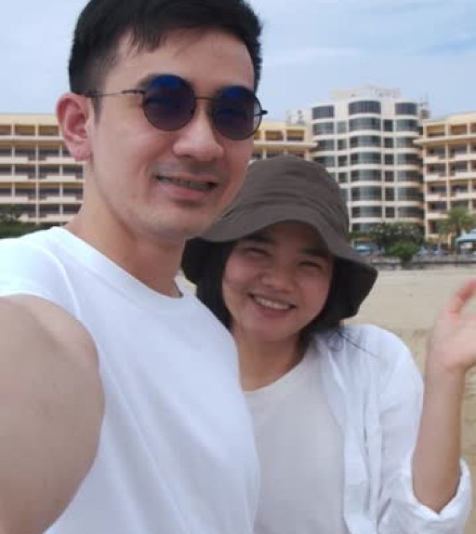 垂直视频: 白人夫妇站在海滩上时向朋友和家人打招呼视频通话，夫妇在旅行期间的夏季假期快乐。