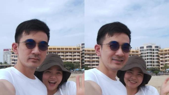 垂直视频: 白人夫妇站在海滩上时向朋友和家人打招呼视频通话，夫妇在旅行期间的夏季假期快乐。