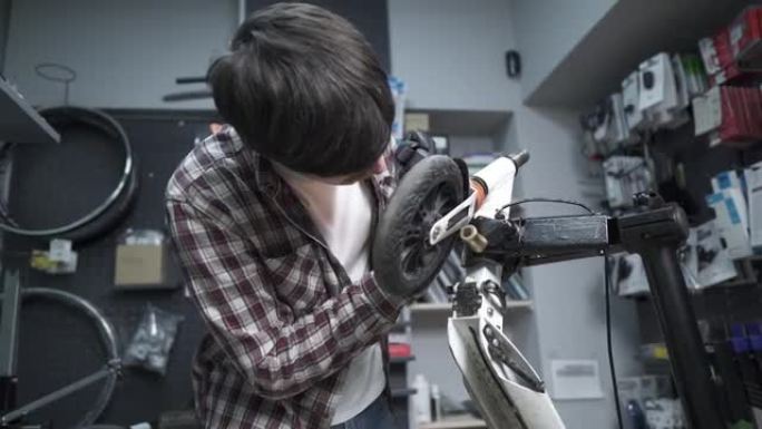 年轻的白人男性机械师在修理厂工作，修理孩子们踢踏板车。修理滑板车，维修服务。生态运输。在特殊车间修理