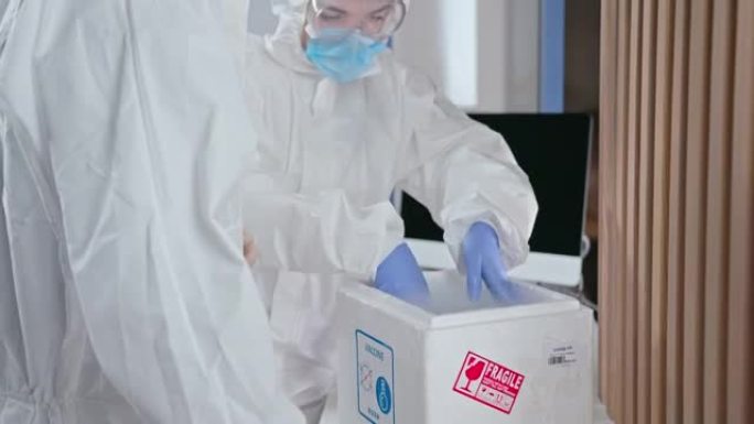 将冠状病毒疫苗交付给疫苗接种部门，穿着防护服的医生在装有制冷剂的热箱中运输一定剂量的现代疫苗