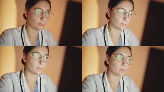 一个女人的脸在电脑上工作的特写镜头。它从灯熄灭开始，然后被监视器发出的光照亮。电脑开机。