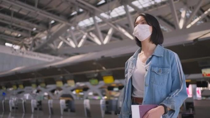 在COVID大流行期间，戴着口罩的女乘客在机场航站楼走到登机口，以防止冠状病毒感染。飞机运输概念中的