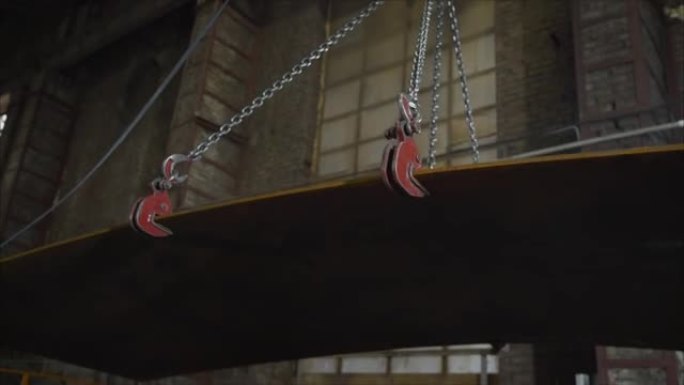 用吊梁移动重型钣金，背景是生产部门的内部。金属板在工厂用起重机吊起。冶金厂。