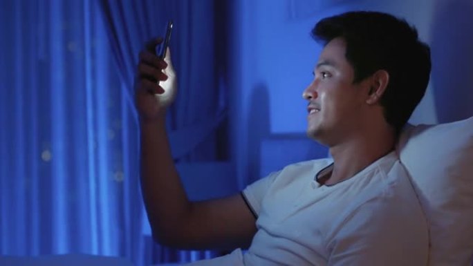 亚洲男子虚拟欢乐时光在线会议与他的女友一起在视频会议中与智能手机一起在晚上睡个好觉，在视频通话中进行