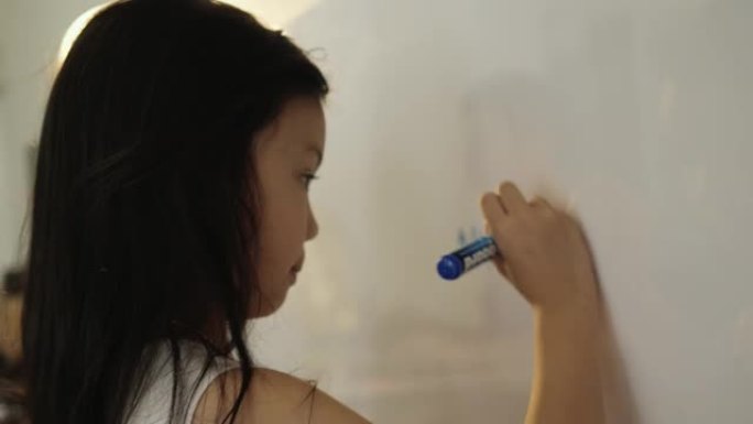 快乐的亚洲女孩在家上学的时候在白板上写答案，生活方式的概念。