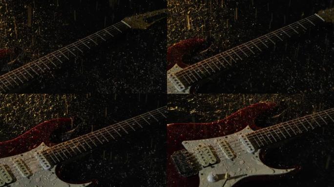 相机在电吉他上滑动，位于黑暗工作室中被黄光照亮的水面上。闪亮的雨滴落在仪器和水上，产生细小的喷雾。特
