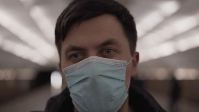 戴着新型冠状病毒肺炎面具的特写男子看着相机。地铁站。电晕病毒。地铁，男性戴着医用口罩悲伤不安，冠状病
