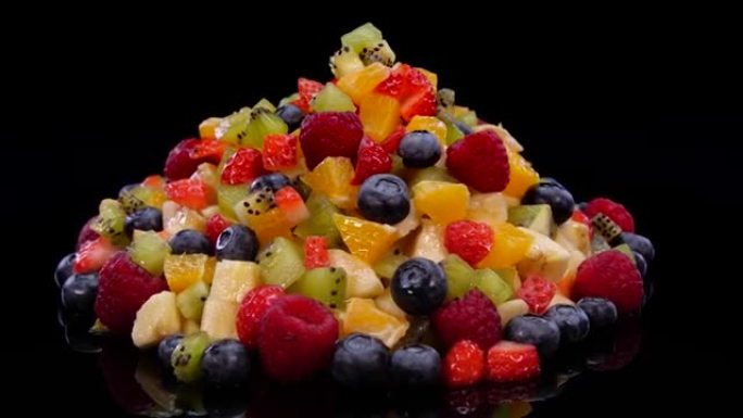 彩色水果沙拉在4k的黑色背景上旋转。关闭新鲜和美味的沙拉，包括橙子，苹果，浆果，石榴，猕猴桃，ana