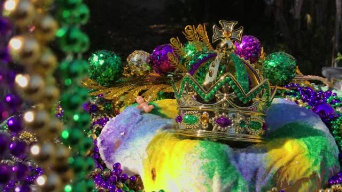Mardi Gras国王蛋糕用串珠围起来，蛋糕上戴着皇冠，小婴儿被五颜六色的珠子围起来