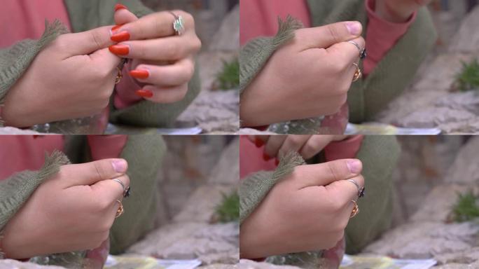 人用覆盖着假宝石的金银戒指去除手指上的假指甲，特写。在家用自己的手修指甲