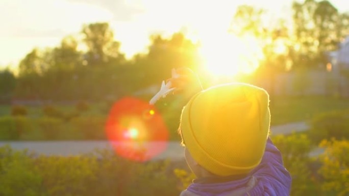 快乐的小男孩在日落时手持玩具飞机在公园里。带飞机的孩子在户外的夏天。小飞行员梦想飞行，旅游度假幸福家