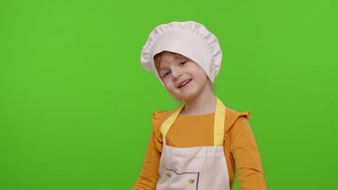 有趣的儿童女孩孩子穿着厨师长贝克围着围裙和帽子跳舞，鬼混，做鬼脸