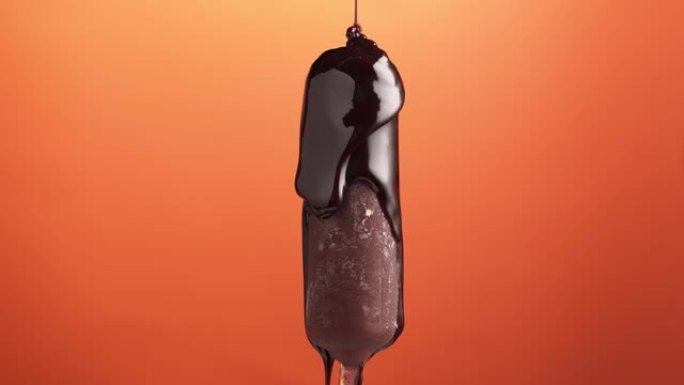 棍子上的冰淇淋，在橙色背景上涂有巧克力釉，旋转。美味的自制冰棒，浇上巧克力浇头。