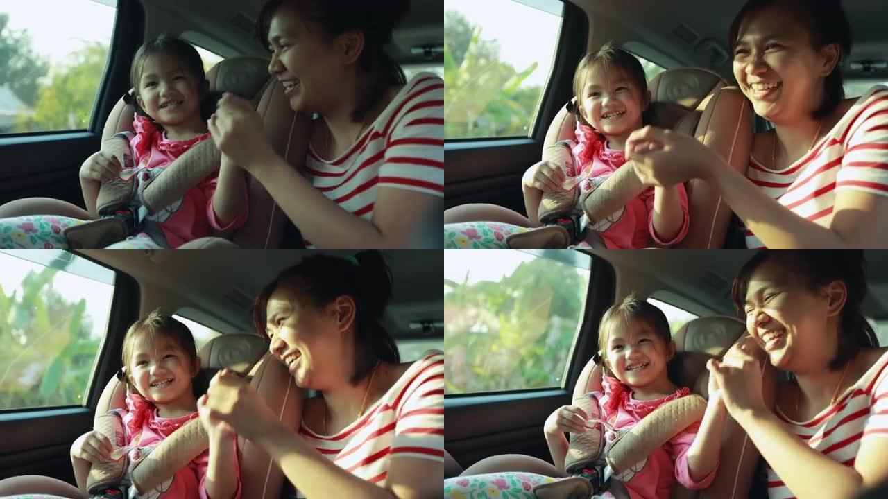 可爱的亚洲小女孩坐在汽车座椅上，她的年轻母亲唱了一首歌，并在慢动作拍摄中带着乐趣和幸福在汽车上一起玩