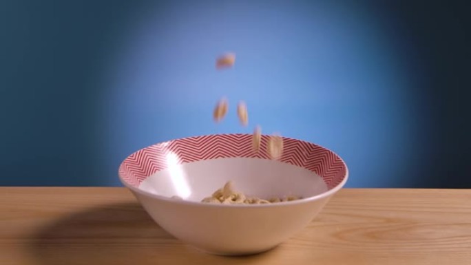 玉米圈形式的早餐谷物掉落并装满碗放在桌子上。食物在蓝色背景上关闭。玉米片和乳制品。美味的配料。健康谷