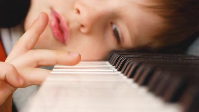 厌倦了课程，一个高加索男孩把头放在钢琴键盘上，用手指弹奏。一个沮丧的学龄前儿童在音乐课后休息。选择性