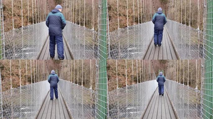 男子在苏格兰肯顿 (Kendoon) 的德河 (River Deugh) 上的吊桥上行走
