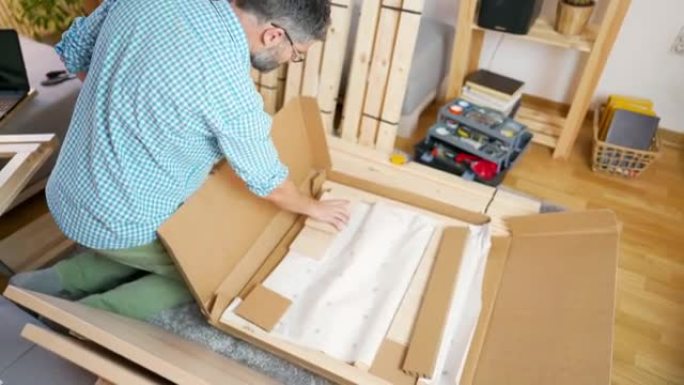 一名成年男子在家中打开装有新家具的纸板箱