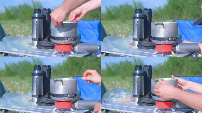 人类在大自然露营时使用小型燃气燃烧器烹饪食物，双手特写。