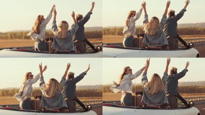 举起手来的快乐朋友在敞篷车里玩得开心。没有车顶的汽车的后视图，在高速公路上，朋友们举手骑在天空上。周
